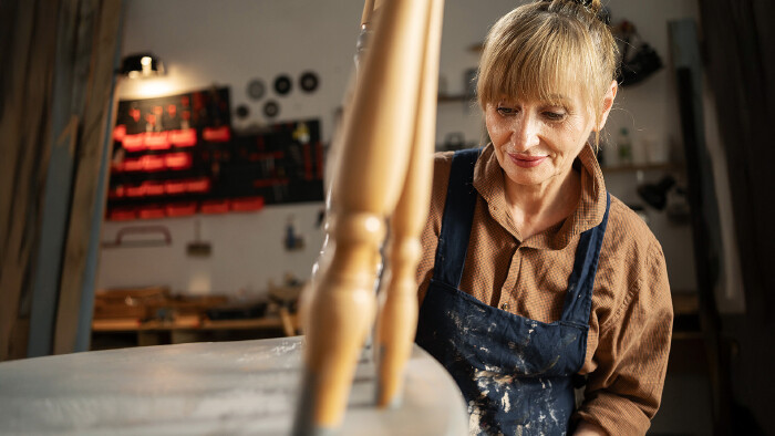 © Andrii Lysenko, stock.adobe.com Eine ältere Tischlerin restauriert einen alten Stuhl.