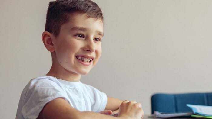 Portr&auml;t eines kleinen, gl&uuml;cklichen Jungen mit Zahnspange, der Online-Videounterricht am Laptop hat