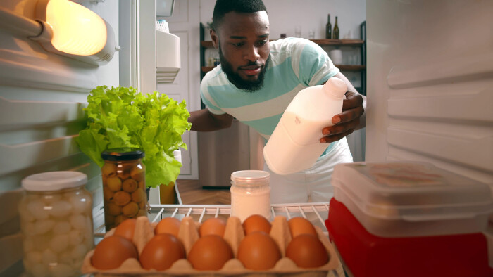 © TommyStockProject, stock.adobe.com Ein afrikanischer Mann nimmt eine Flasche Milch aus dem vollen Kühlschrank