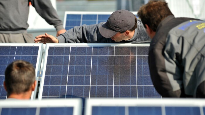 4 junge Männer montieren Sonnenkollektoren auf einem Dach.
