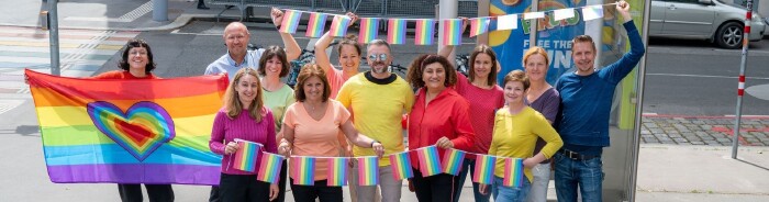 AK Präsidentin Renate Anderl und 8 Mitarbeiter:innen der AK Wien gehen in bunten T-Shirts über einen Regebogen-Zebrastreifen und lachen in die Kamera