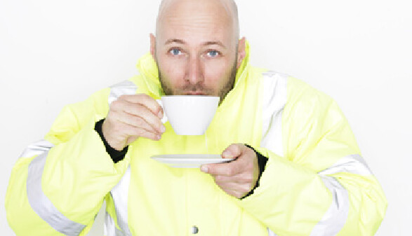 Ein Mann in Arbeitskleidung nippt an einer Tasse Tee, in der anderen Hand hält er die Untertasse.