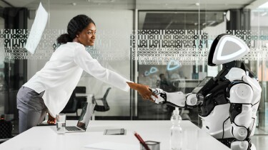 Businessfrau reicht im B&uuml;ro einem sitzenden Roboter die Hand