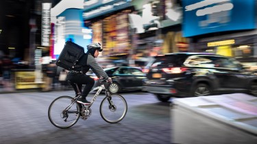 Radzusteller radelt über den im Hintergrund verschommen sichtbaren New Yorker Timesquare © Unsplash - Brett Jordan