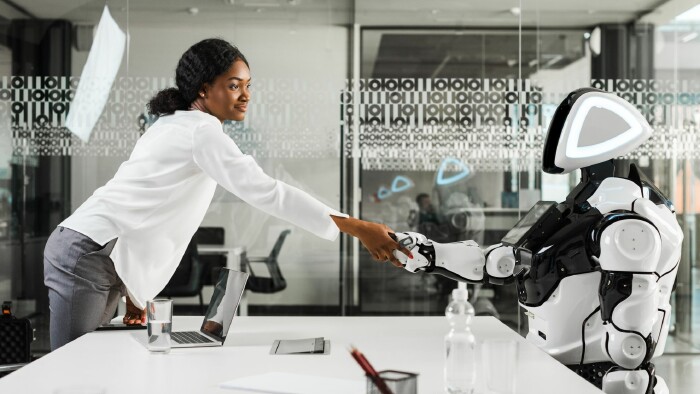 Businessfrau reicht im B&uuml;ro einem sitzenden Roboter die Hand