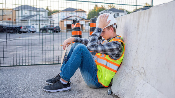 Junger Bauarbeiter mit Schutzhelm sitzt auf dem Boden.