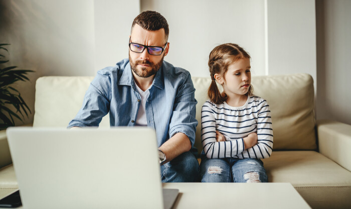 Vater und Kind sitzen zu Hause auf der Couch. Vater besch&auml;ftigt sich mit Laptop.