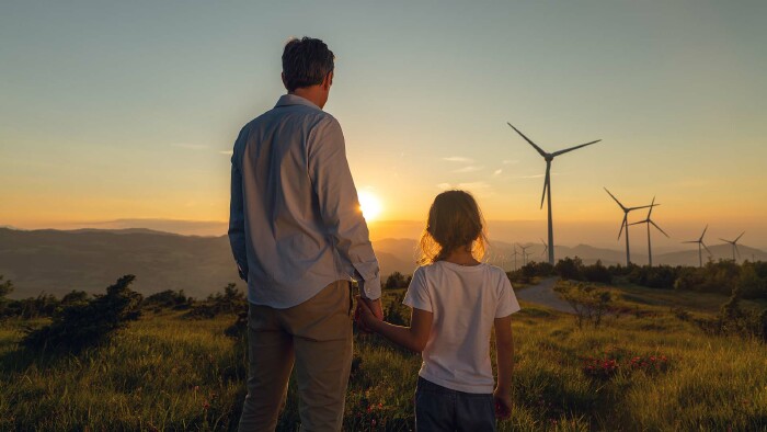 Vater mit Tochter. Beide blicken auf eine Landschaft. Windr&auml;der sind zu sehen.