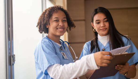 Zwei Frauen in medizinischer Arbeitskleidung lachen in die Kamera