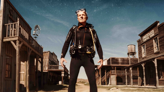 Thomas Maurer steht in einem Taucheranzug in der Mitte einer leeren Wild West-Stadt, hinter ihm ein Sternenhimmel.