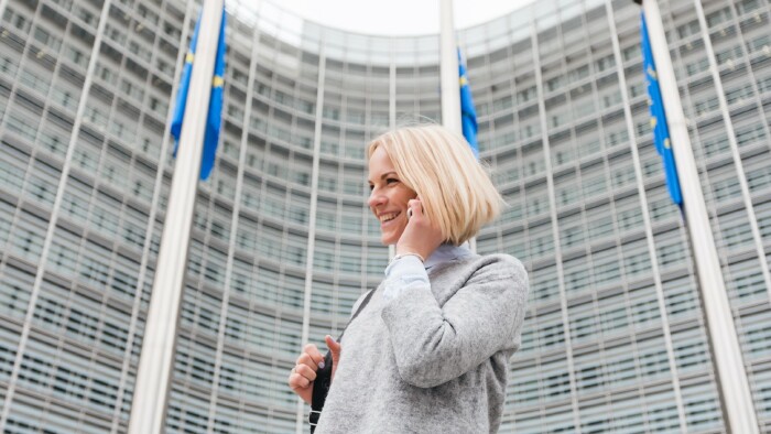 Eine junge Frau spaziert mit dem Handy in der Hand an der Europ&auml;ischen Kommission vorbei.