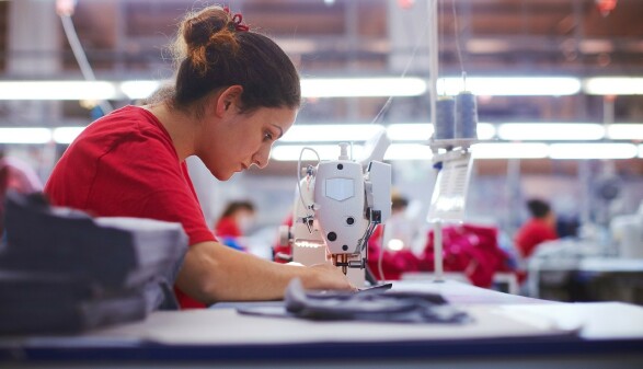  Junge Schneiderin arbeitet an einer N&auml;hmaschine in einer Textilfabrik