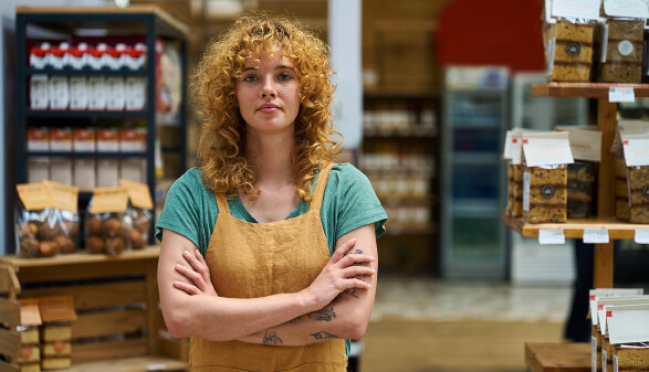 Selbstbewusste Verk&auml;uferin steht mit verschr&auml;nkten Armen im Supermarkt.