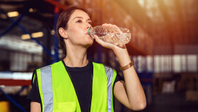 Arbeiterin trinkt auf der Baustelle Wasser aus einer Flasche