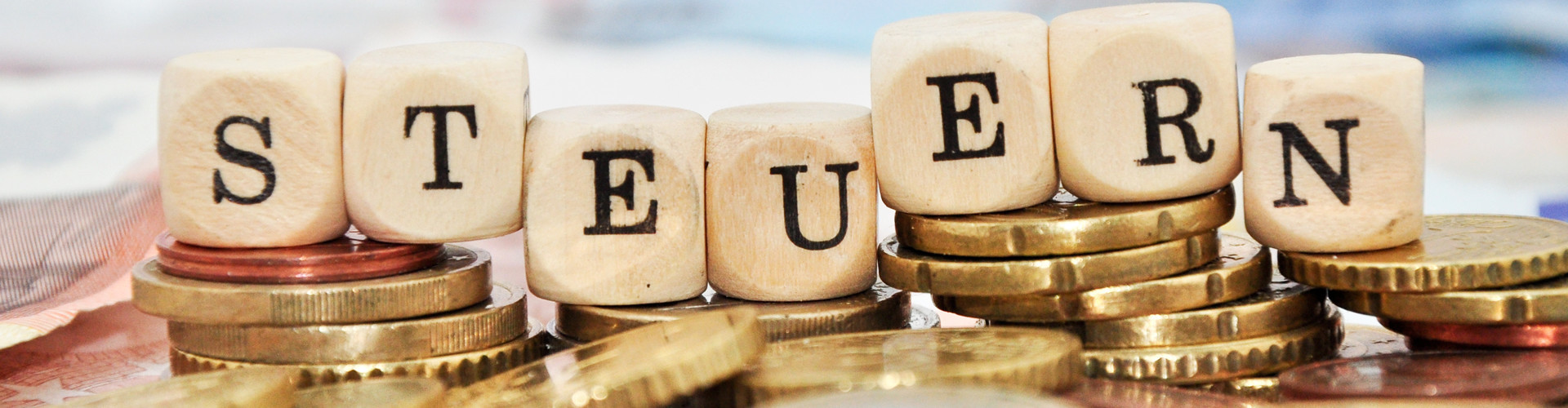 Buchstabenwürfel, welche auf einem Stapel Euro-Münzen liegen, bilden das Wort "Steuern" © Marco2811, stock.adobe.com