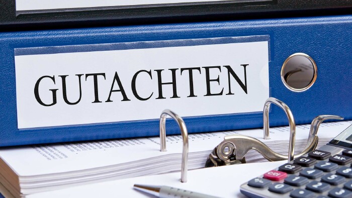 Ein Aktenordner mit der Aufschrift GUTHABEN, ein Taschenrechner und ein Kugelschreiber liegen auf einem Tisch.