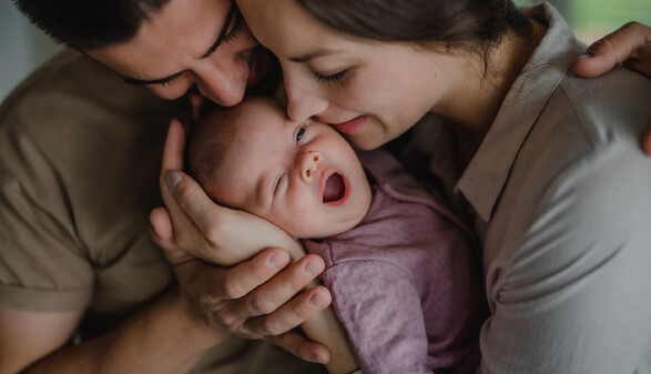 Eltern halten ein neugeborenes, gähnendes Baby zärtlich im Arm