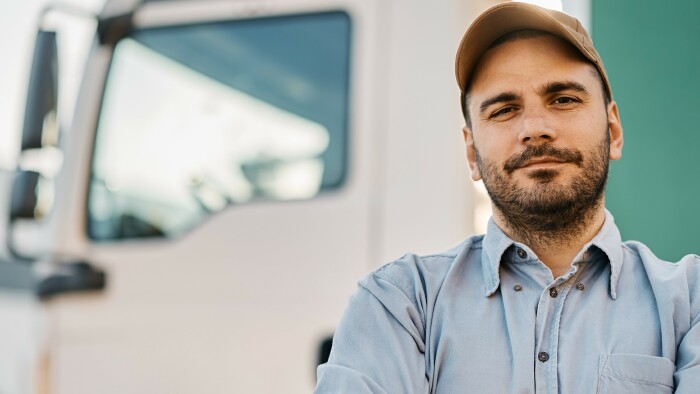 © drazen zigic, stock.adobe.com Lkw-Fahrer steht mit verschränkten Armen vor seinem Lkw.