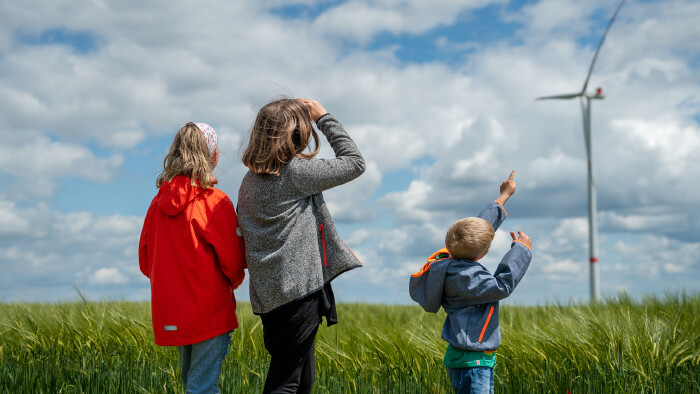 Kinder stehen auf einer Wiese vor einem Windrad und symbolisieren spielerisch die Energiewende und eine nachhaltige Zukunft.