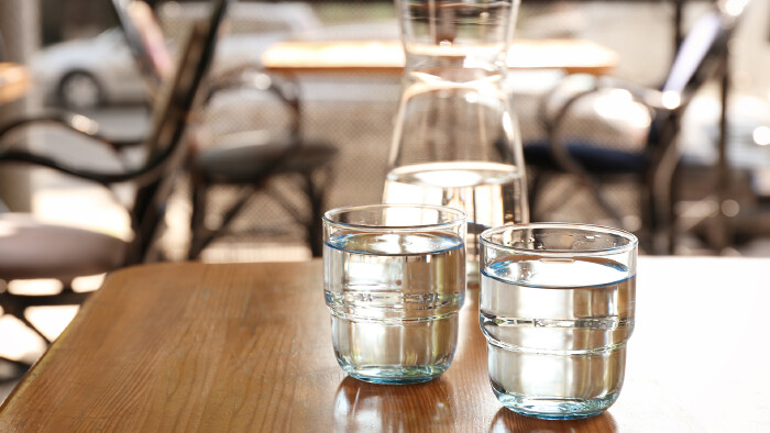 Zwei Gl&auml;ser Wasser auf einem Tisch in einem Restaurant. Dahinter ist eine Karaffe mit Wasser zu sehen.