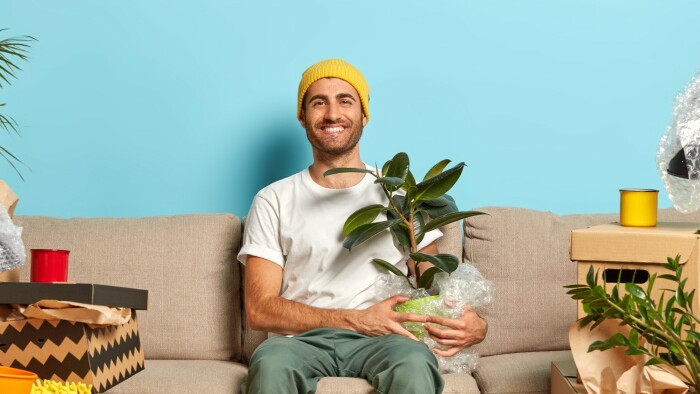 Junger, zufriedener Mieter sitzt in der neu bezogenen Wohnung auf einem beigen Sofa. 