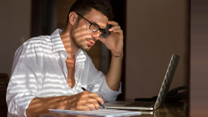 Mann mit Brille sitzt bei Notebook und &uuml;berlegt