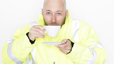 Ein Mann in Arbeitskleidung nippt an einer Tasse Tee, in der anderen Hand hält er die Untertasse.