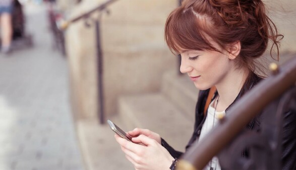 Junge Frau sitzt draußen auf einer Treppe und schaut auf ihr Handy