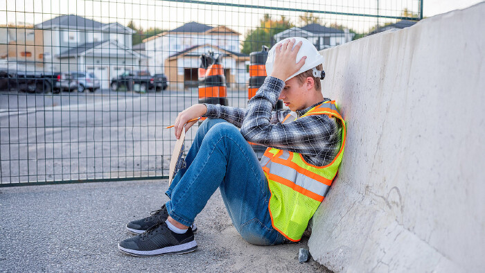 Junger Bauarbeiter mit Schutzhelm sitzt auf dem Boden.
