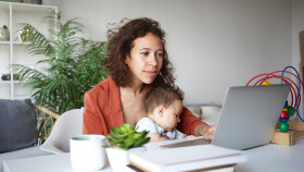 Frau mit Baby am Schoß arbeitet am Laptop