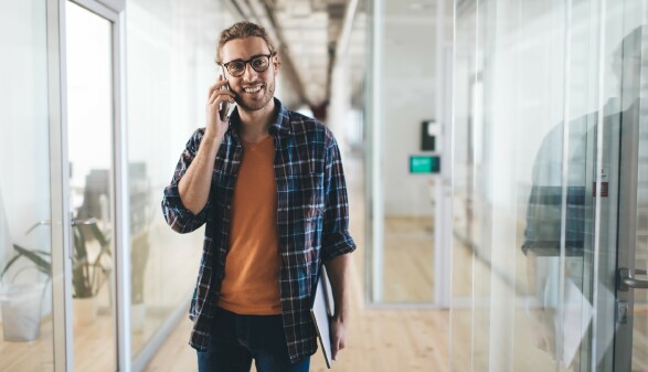 Junger Mann mit Laptop, der während der Arbeit telefoniert