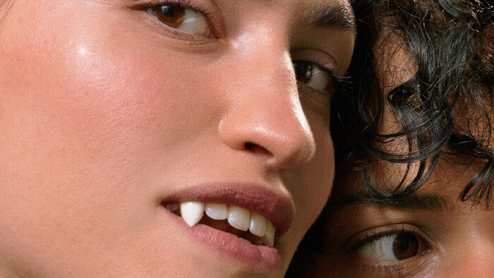 Junge Frau mit Vampirz&auml;hnen schaut in die Kamera, hinter ihr sieht man angeschnitten das Gesicht eines anderen M&auml;dchens.