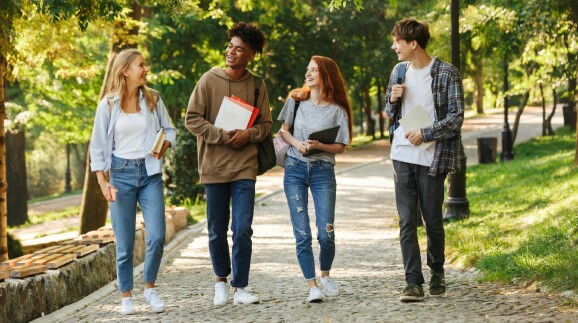  Gruppe gl&uuml;cklicher Student:innen, die auf dem Campus spazieren gehen