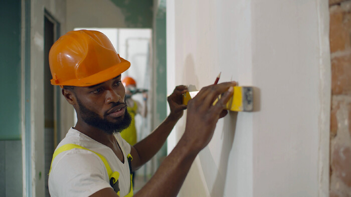 © TommyStockProject, stock.adobe.com Afrikanischer Arbeiter auf der Baustelle mit einer Wasserwaage in der Hand